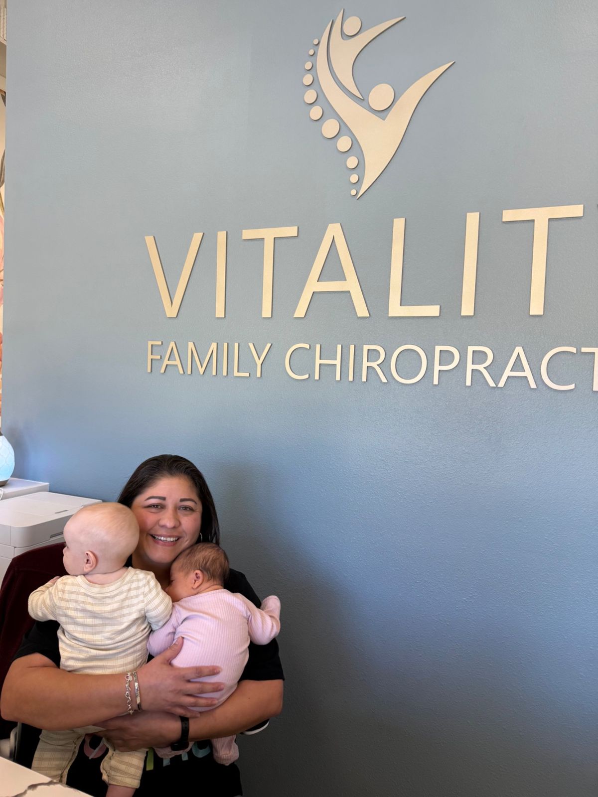 A team member holds two babies beneath the Vitality Family Chiropractic sign