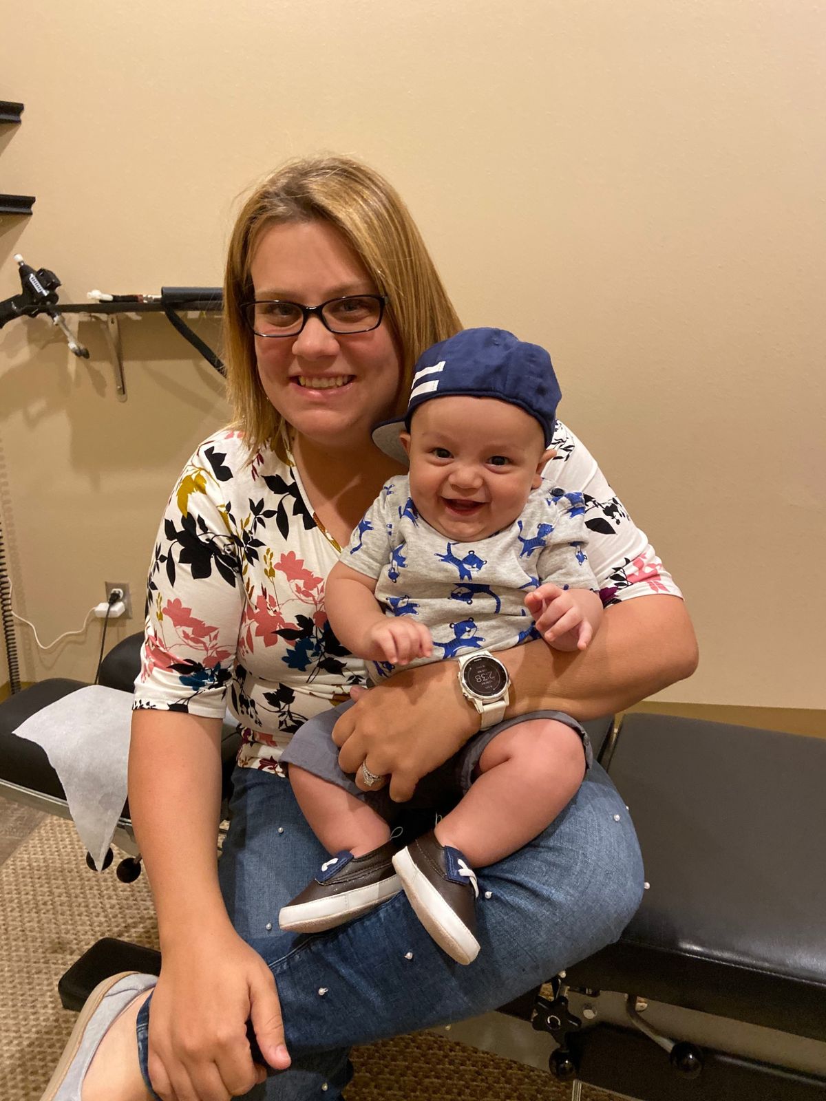 A smiling mom holds her grinning baby, who is wearing a ball cap