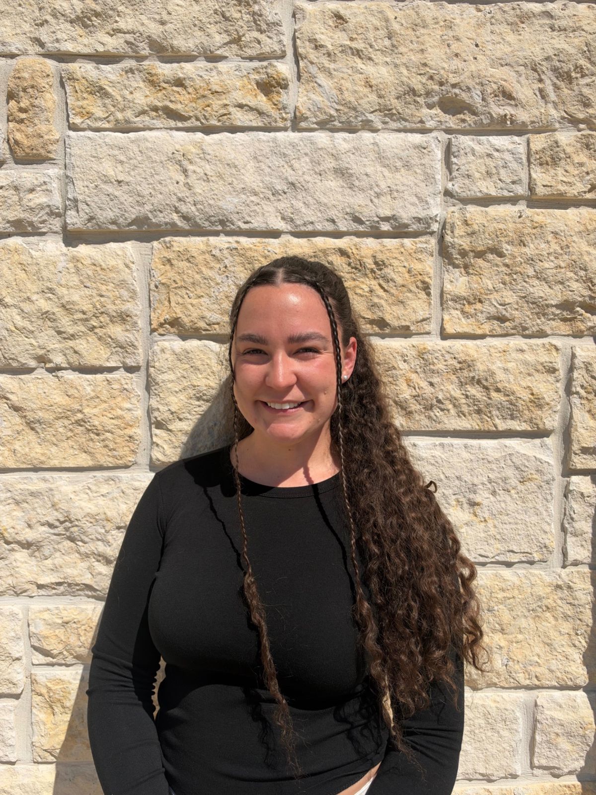 Dr. Mikah smiling in front of a stone wall