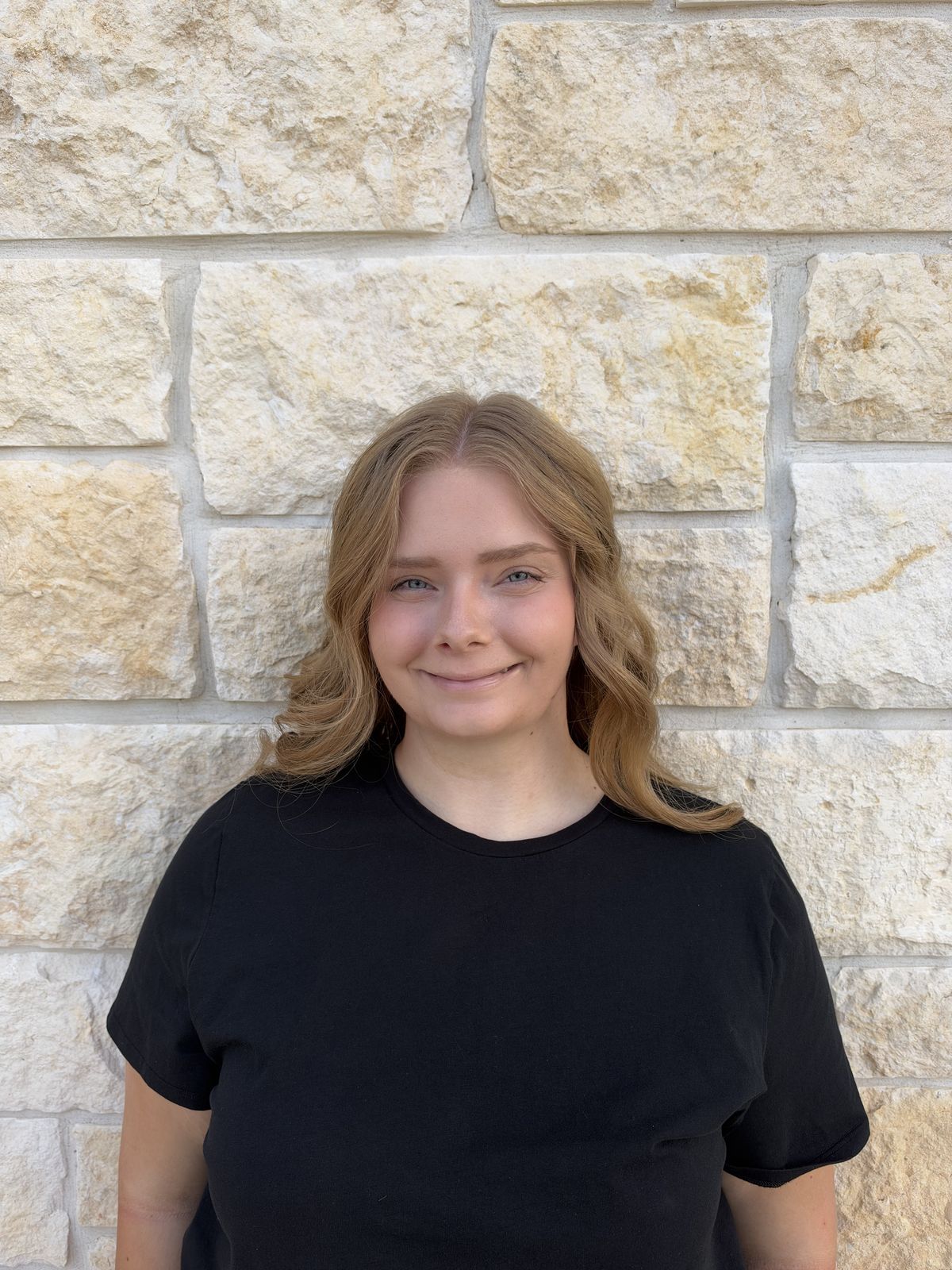 Mikayla smiling in front of a stone wall